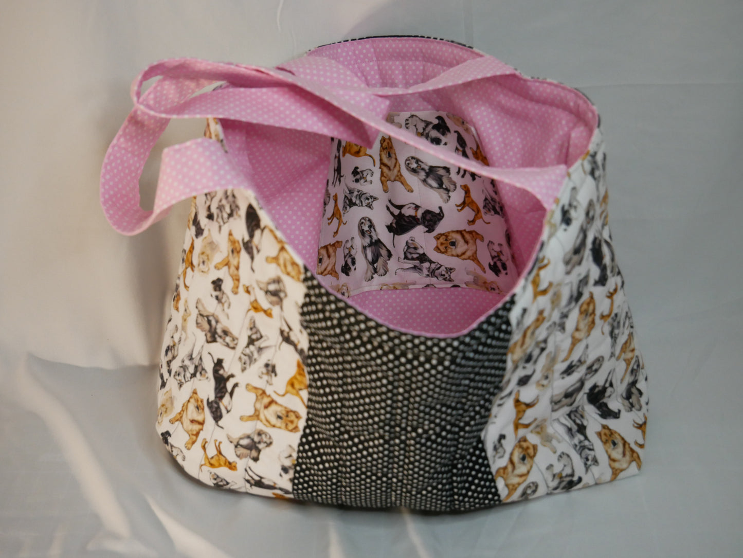 A handmade fabric boxy tote bag with pink polka-dot handles and interior with a dog themed fabric in black, white and and golden brown .