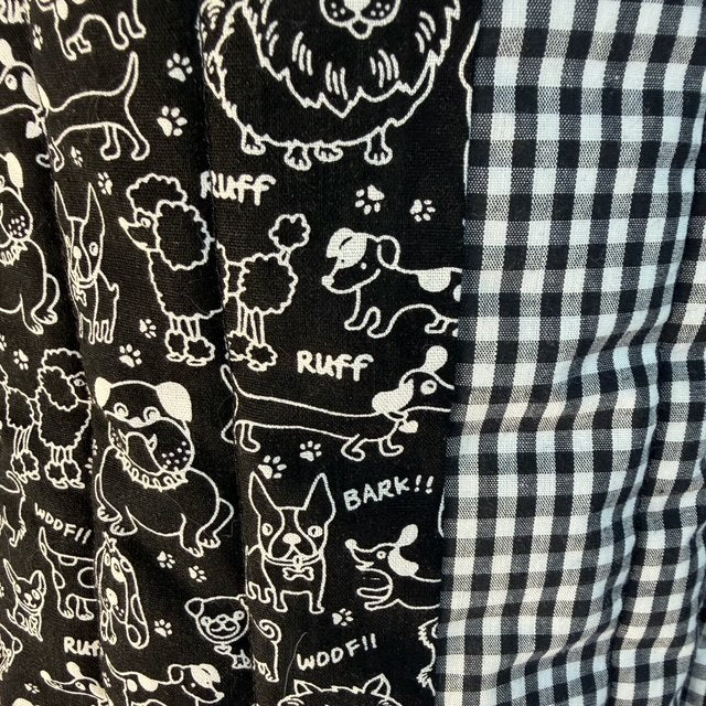 Close-up of a fabric product showing two distinct patterns: a black background with white dog illustrations and text, next to a classic black and white gingham checkered pattern.