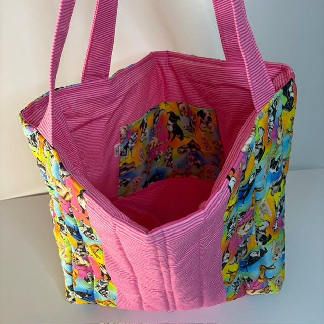A handmade fabric tote bag with a bright pink interior and handles, and colorful dog themed fabric on the sides.