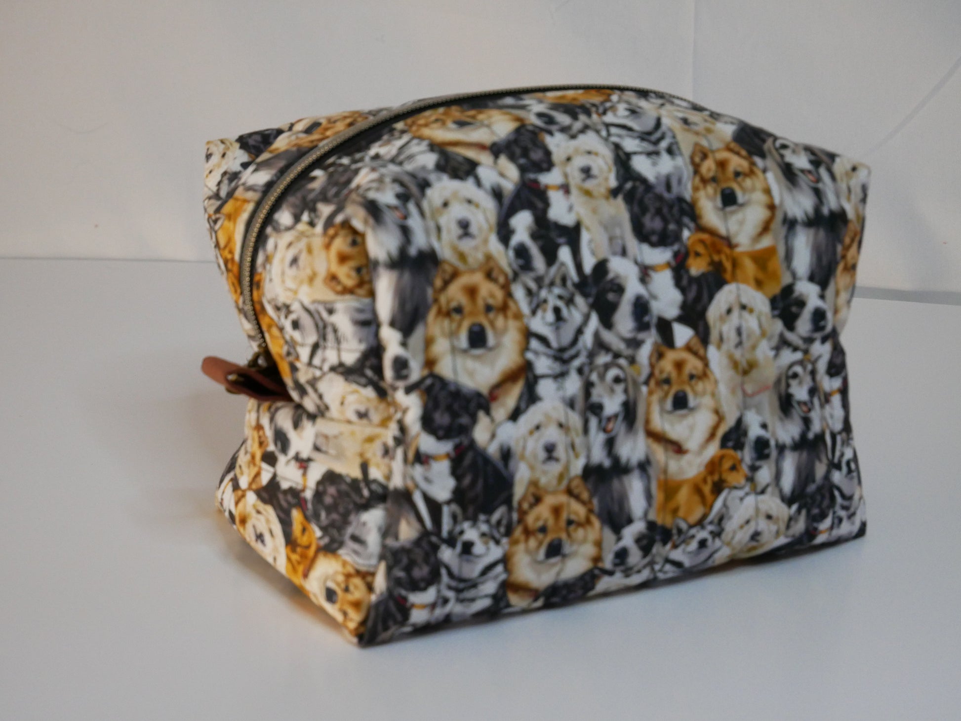 A zippered boxy bag with a dog themed printed fabric in black, white, and orange-brown tones.
