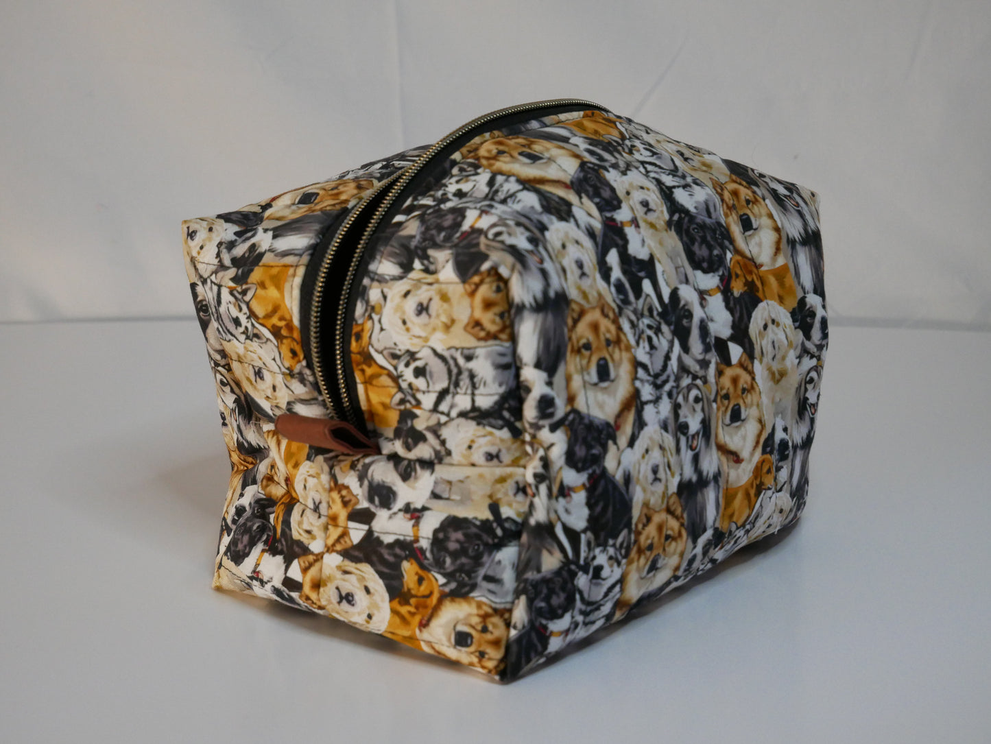 A zippered boxy bag with a dog themed printed fabric in black, white, and orange-brown tones.