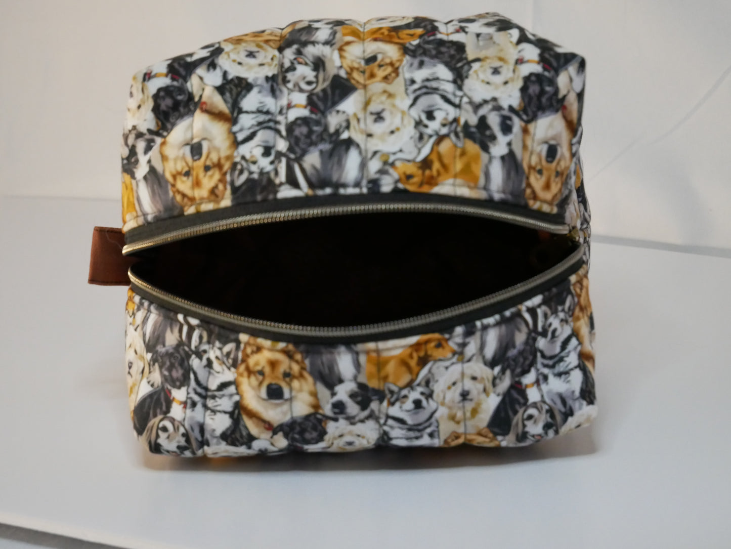 A zippered boxy bag with a dog themed printed fabric in black, white, and orange-brown tones.