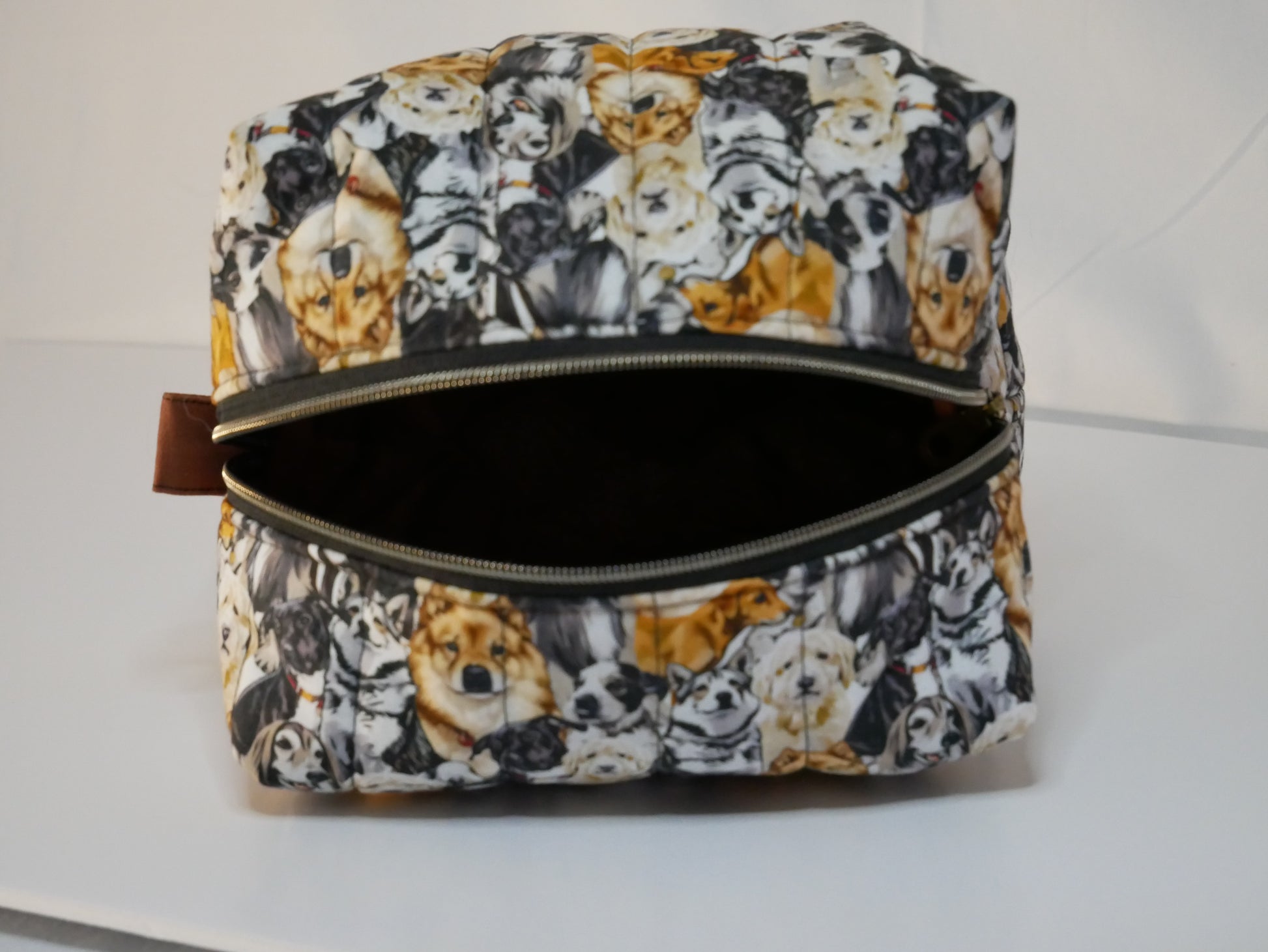 A zippered boxy bag with a dog themed printed fabric in black, white, and orange-brown tones.