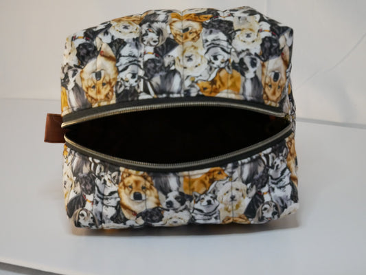 A zippered boxy fabric bag with dog themed printed fabric in black, white and brown tones - used for storing dog tools like brushes, leashes and clippers.