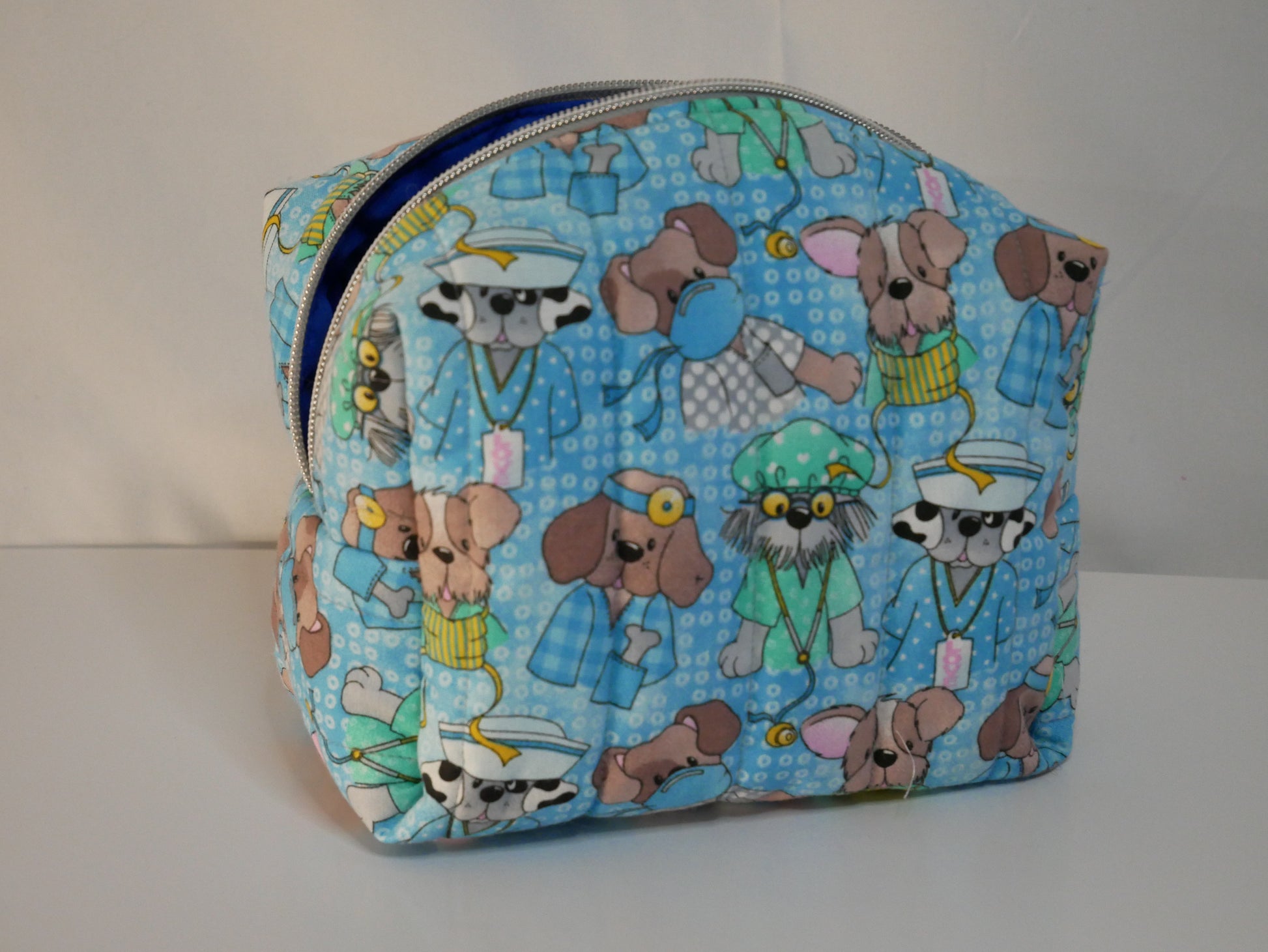 A zippered  boxy bag featuring a light blue background printed with cartoon dogs dressed as doctors and nurses.