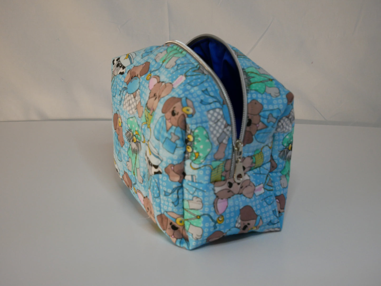 A zippered boxy fabric bag blue background and a doctor and nurse teddy bear pattern, shown open to reveal a blue interior.