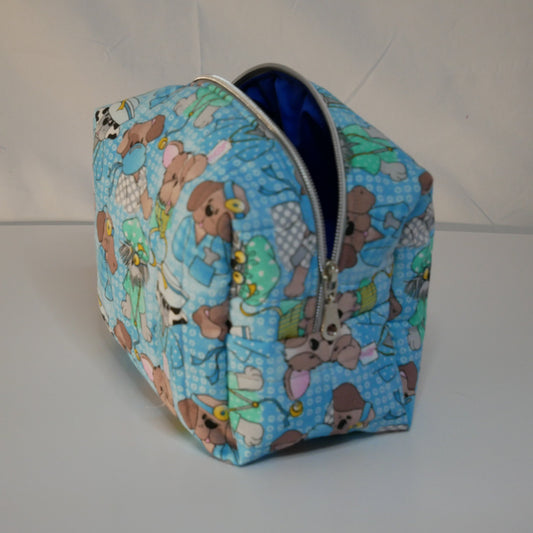 A zippered boxy fabric bag  with a blue background, a doctor and nurse teddy bear pattern, used for storing dog tools like brushes, leashes and clippers.