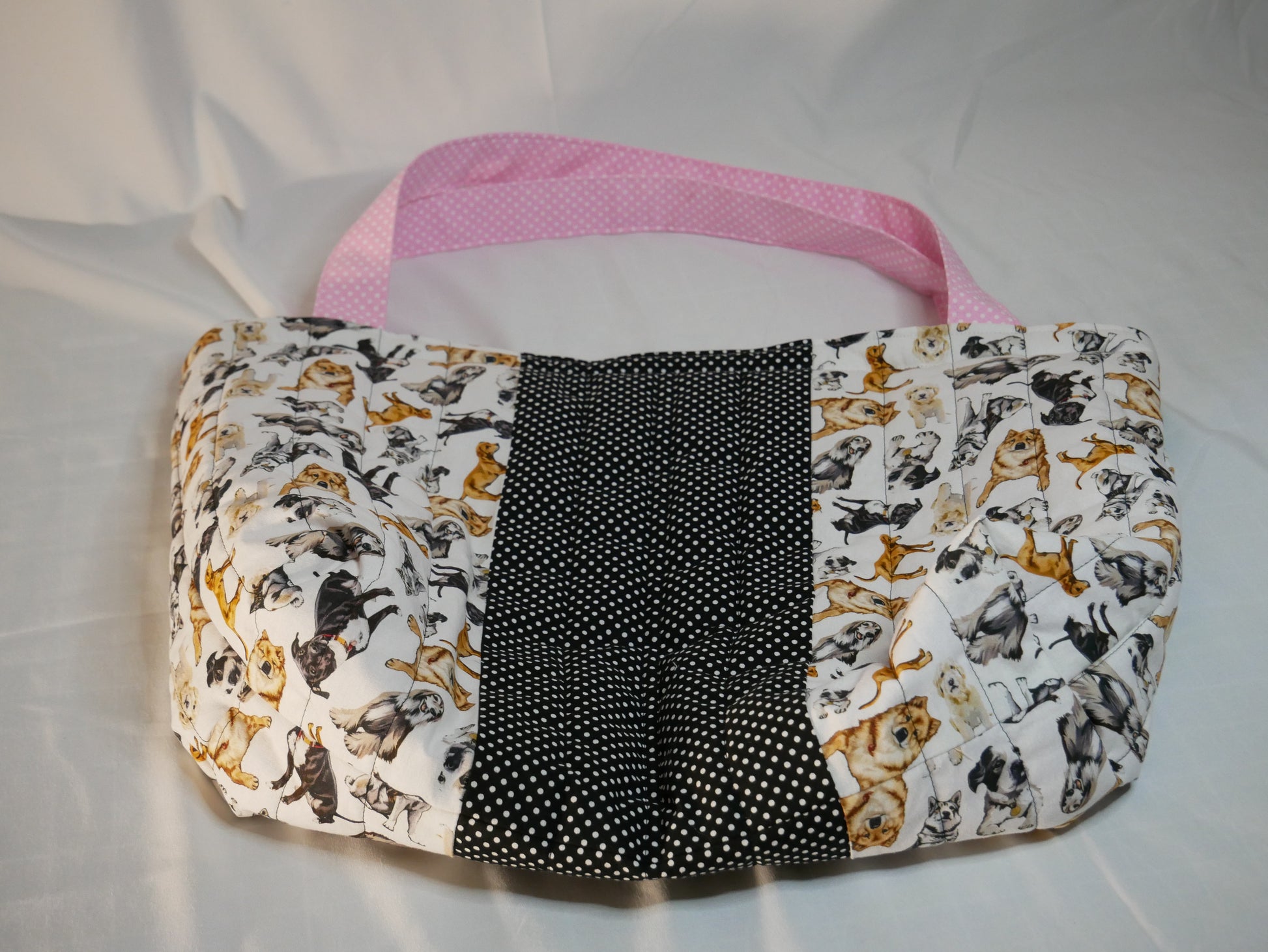 A handmade fabric boxy tote bag with pink polka-dot handles and interior  with a dog themed fabric in black, white and and golden brown .