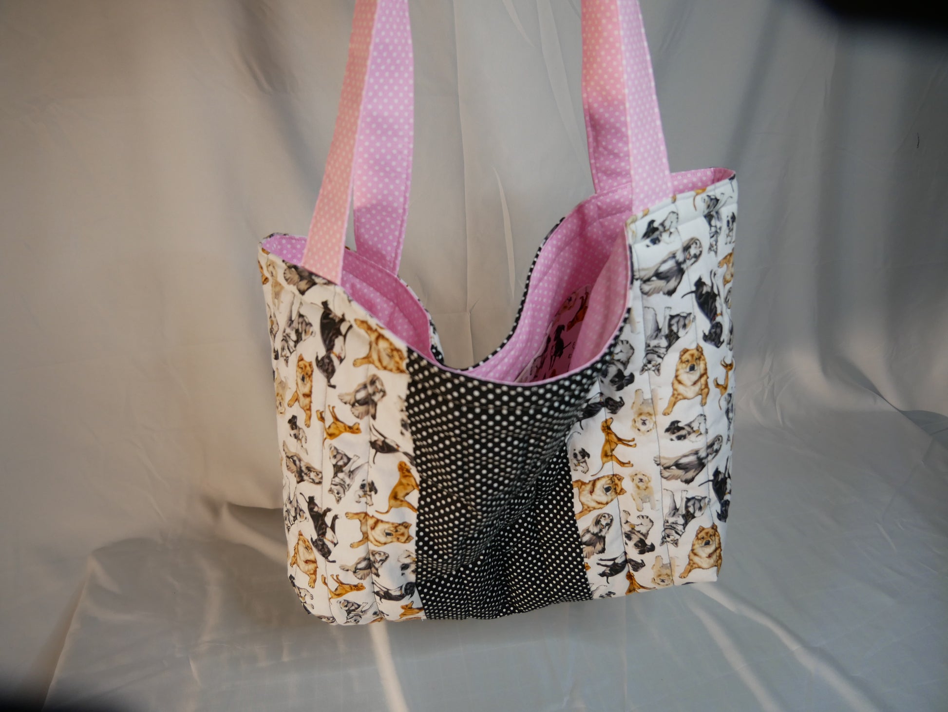 A handmade fabric boxy tote bag with pink polka-dot handles and interior  with a dog themed fabric in black, white and and golden brown .