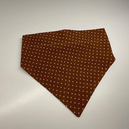 a scrunchie dog bandana  in a chocolate brown patterned fabric with a small white x pattern. 