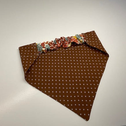 a scrunchie dog bandana  in a chocolate brown patterned fabric with a small white x pattern. 