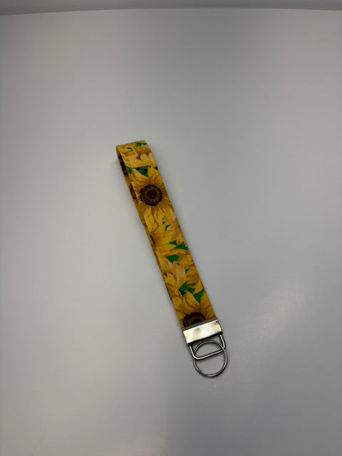 A fabric wristlet keychain in a yellow sunflower pattern with a silver metal clip and keyring.