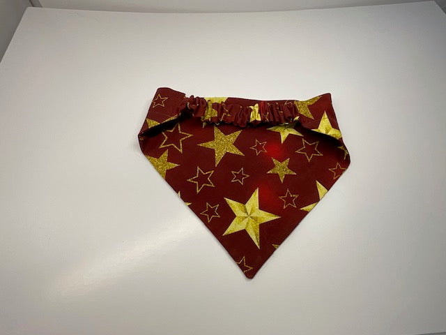 A handmade scrunchie dog bandana sewn with a fabric pattern of gold stars on a red and burgundy fabric - Doggie Dekor