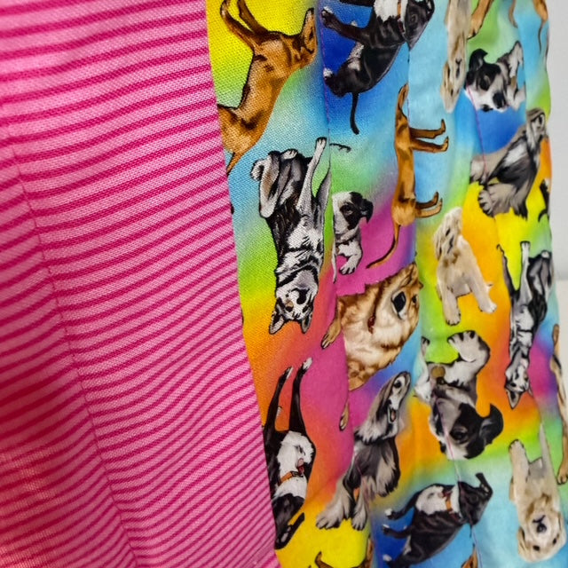 A close-up of fabric showing two different patterns: a solid pink and white striped fabric on the left, and a vibrant multicolor fabric on the right featuring cartoon dogs on a rainbow background.