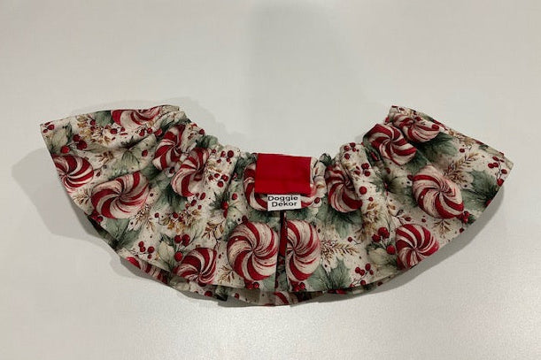 A ruffled pet collar with a festive holiday print of red and white peppermint candies, green holly leaves, and red berries - the neck ruffle by doggie dekor calgary