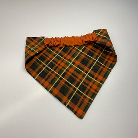 A scrunchie dog bandana with a fall inspired flannel pattern in orange, black, green and a sparkly yellow stripe.
