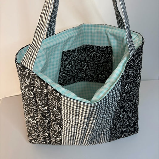 A quilted fabric tote bag with a black and white gingham pattern with black and white dog themed fabric and a teal gingham lining