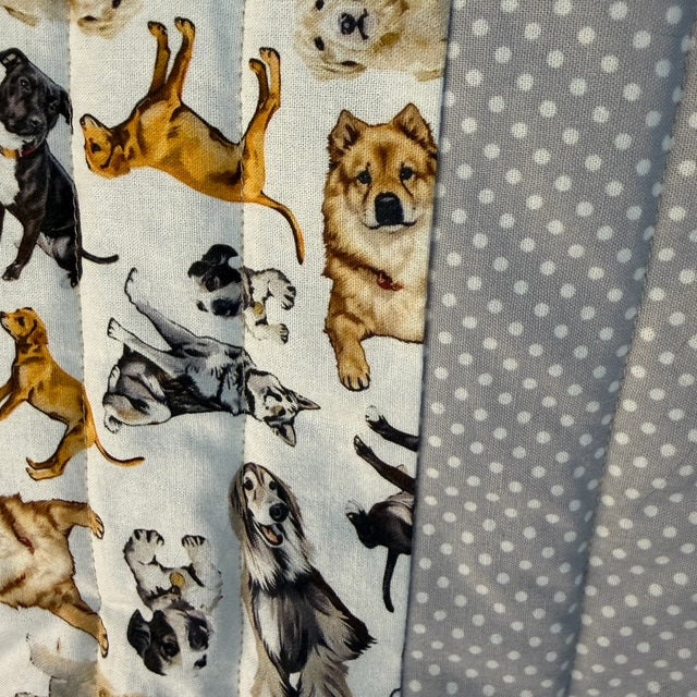Close-up of a quilted fabric featuring a multicolor print of various dog illustrations on a white background, next to a gray fabric with white polka dots.